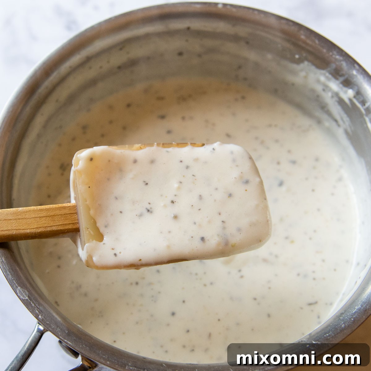 A spoon lifting out a spoonful of thickened, white creamy sauce from a saucepan.