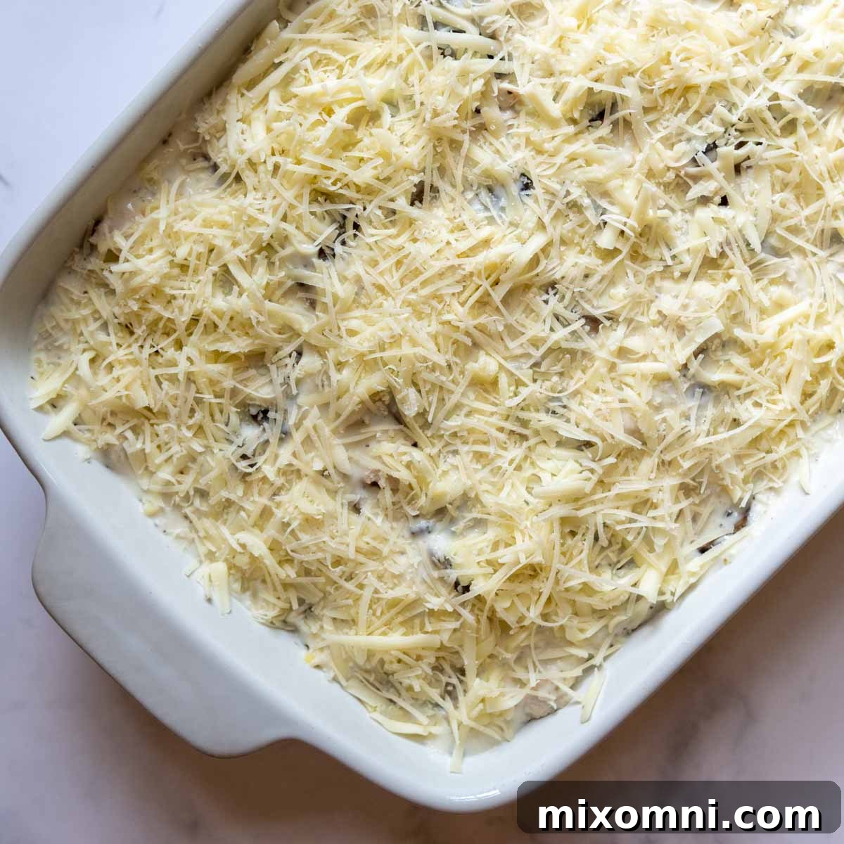 An unbaked gluten-free chicken tetrazzini casserole, topped with cheese, ready for the oven.