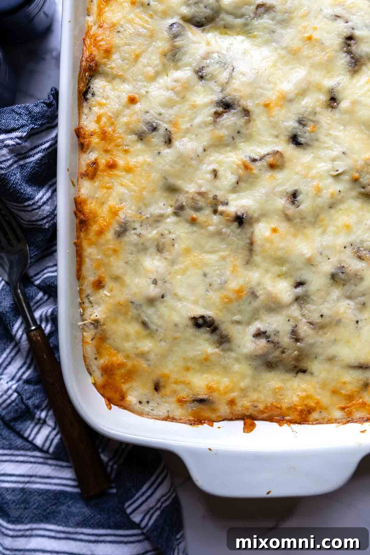 A finished tetrazzini casserole in a white baking dish with a blue napkin nearby, ready to be served.