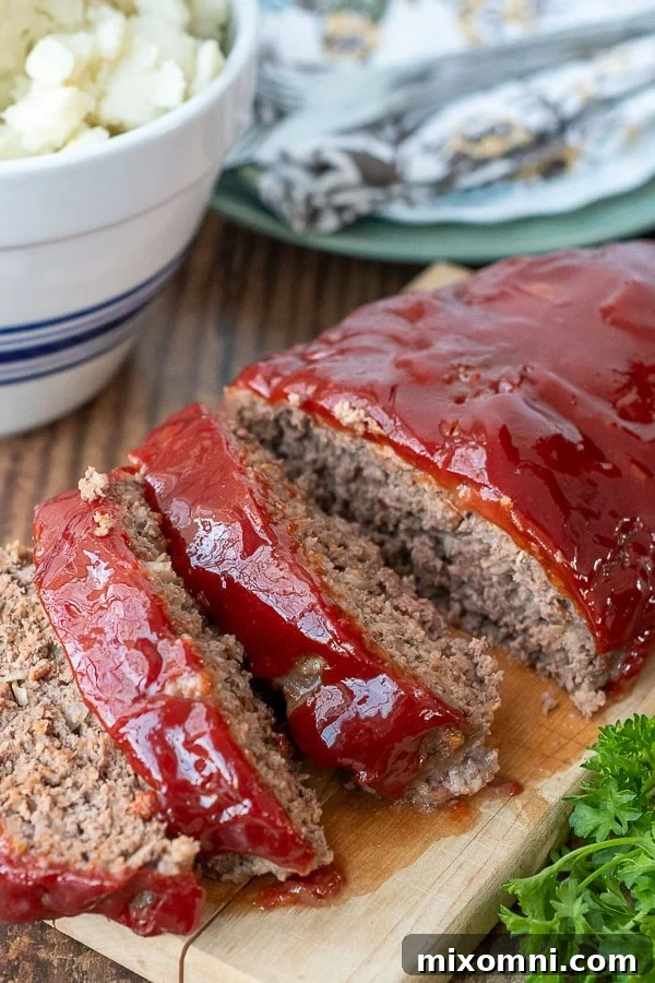 meatloaf sliced on a wooden board with a bowl of mashed potatoes in the background