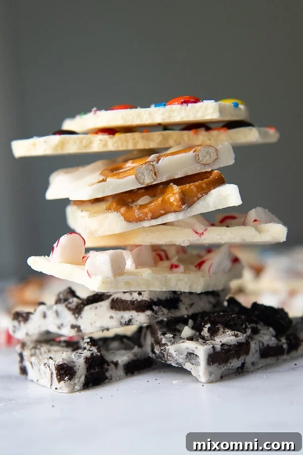 A beautifully arranged stack of various white chocolate bark flavors: Oreo bark, peppermint bark, pretzel bark, and festive Christmas bark, showcasing their diverse textures and toppings.