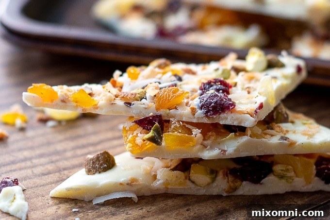 A neatly stacked collection of white chocolate fruit and nut bark pieces, showcasing the vibrant colors of dried fruits and the appealing texture of nuts against the white chocolate.