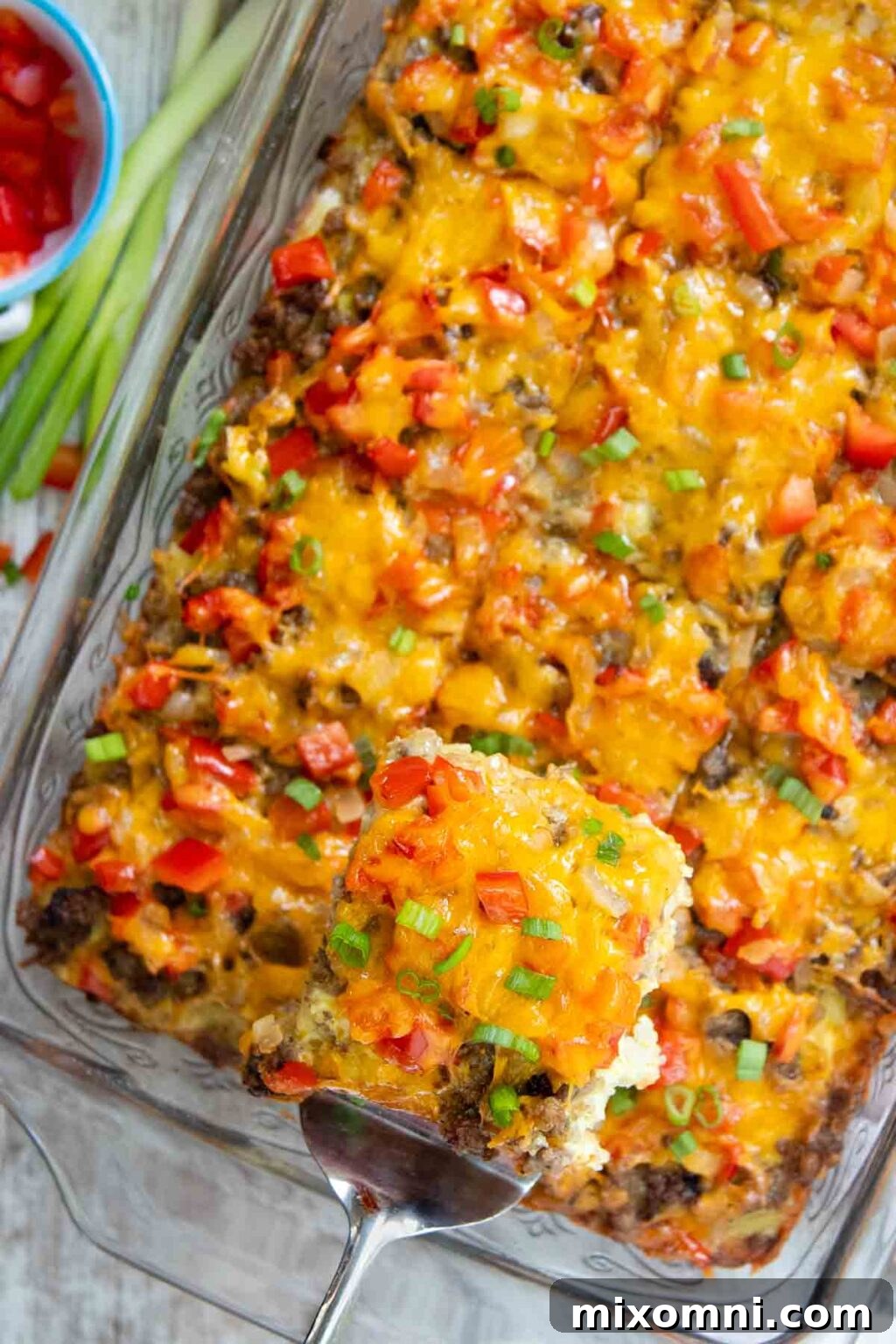 A golden-brown slice of gluten-free breakfast casserole, with visible layers of sausage, hash browns, eggs, and cheese, being lifted from a baking dish with a spatula.