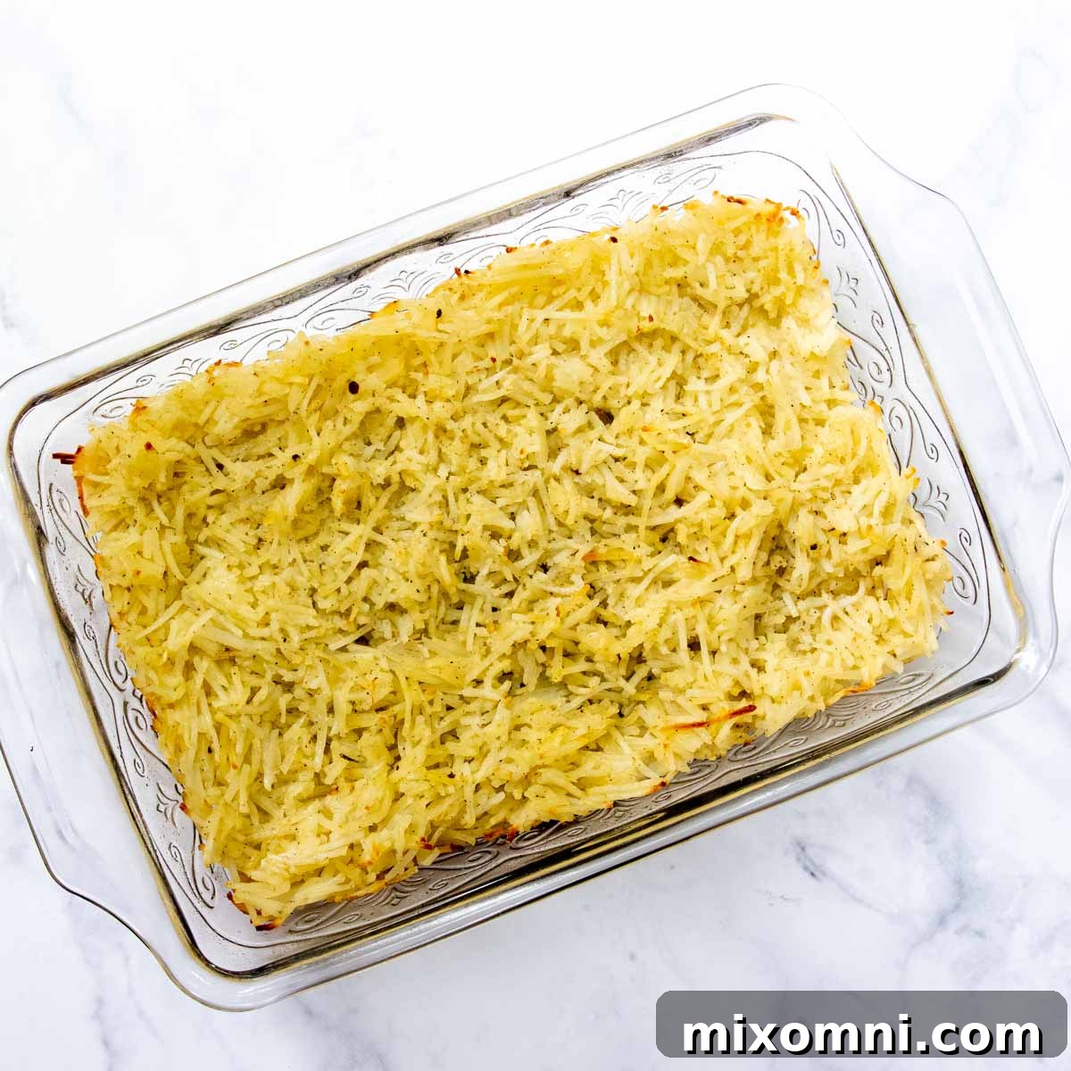 Partially baked hash browns forming a golden crust in a baking dish, ready for the next layer.