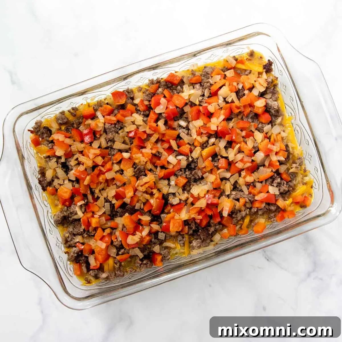 An unbaked breakfast casserole, topped with a final layer of shredded cheese, ready to be placed in the oven.