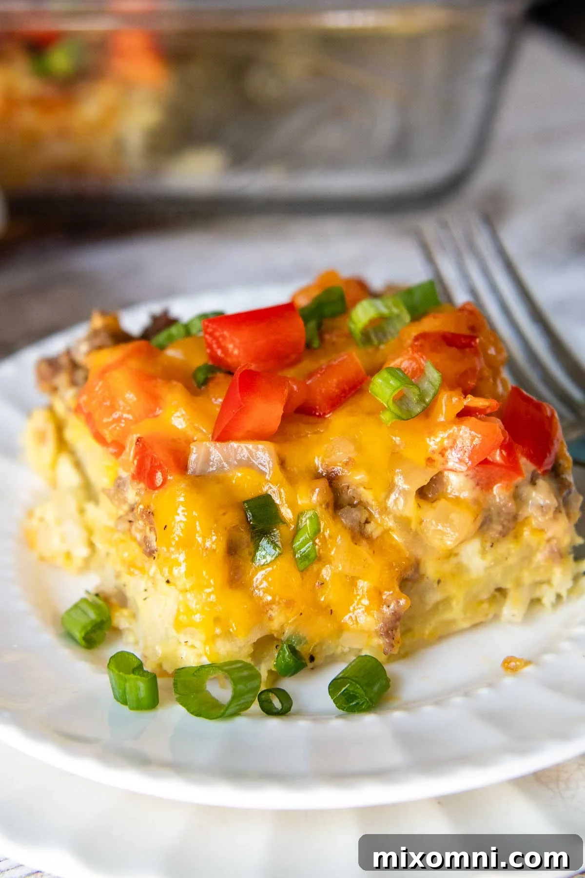 A perfectly portioned slice of gluten-free breakfast casserole on a white plate, garnished with fresh green onions, highlighting its golden crust and delicious layers.