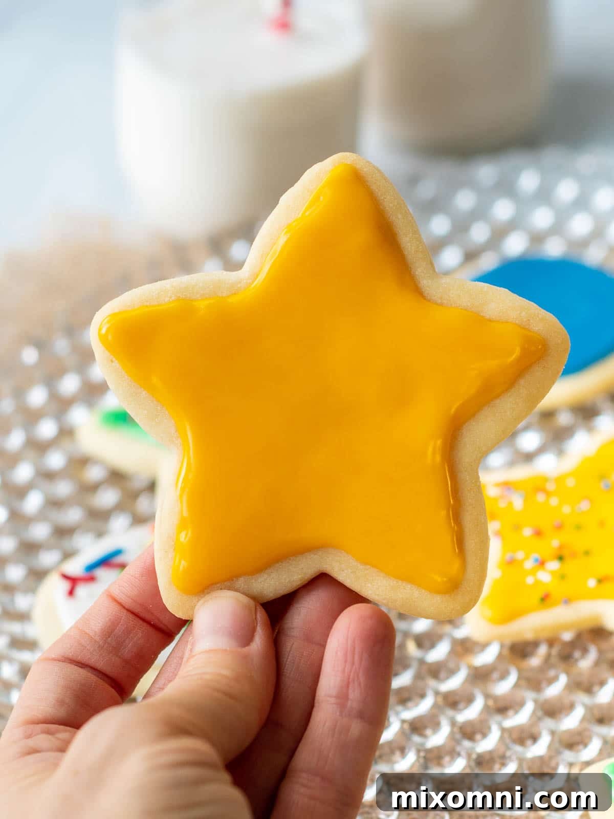 A golden-yellow star-shaped sugar cookie, perfectly iced and glistening, being held up to showcase its glossy finish and intricate details. The icing has set firm, reflecting light beautifully.