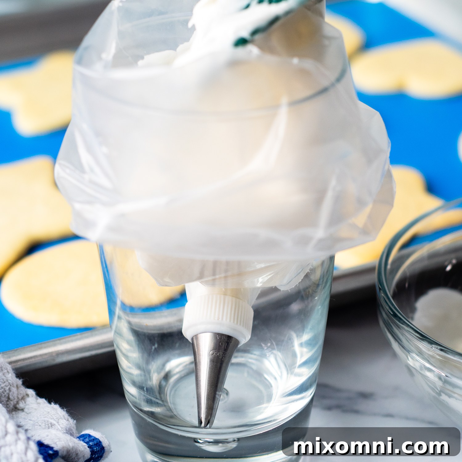 Thick, white sugar cookie icing being neatly scooped into a clear plastic piping bag, ready for intricate cookie decorating.