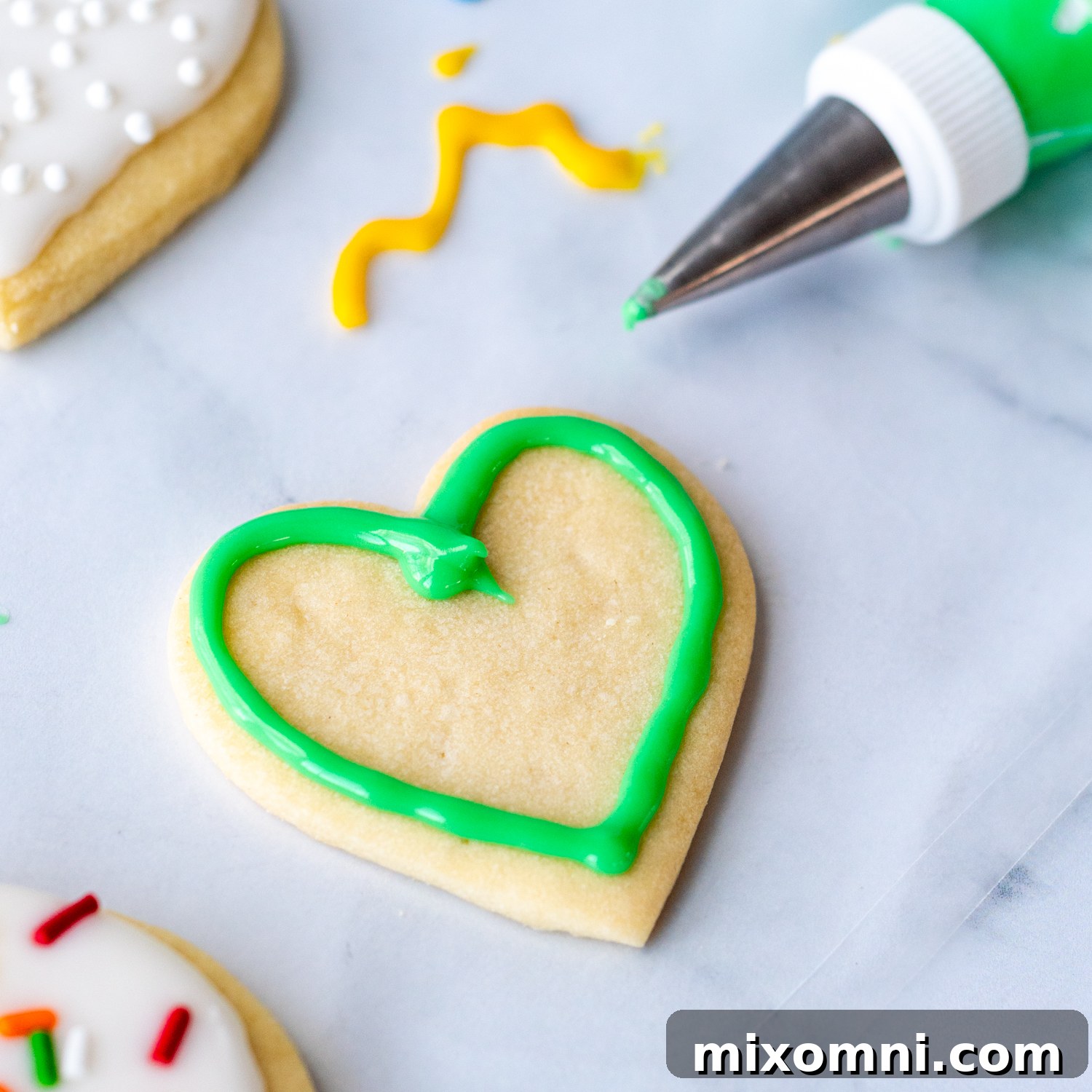 A heart-shaped sugar cookie outlined with a crisp green frosting border, demonstrating the first step in the flooding technique for cookie decorating.