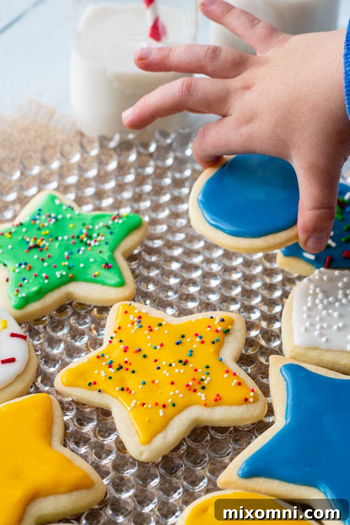 A child's hand reaching for a vibrant green star-shaped sugar cookie, beautifully decorated with glossy icing, illustrating the joy of homemade treats.