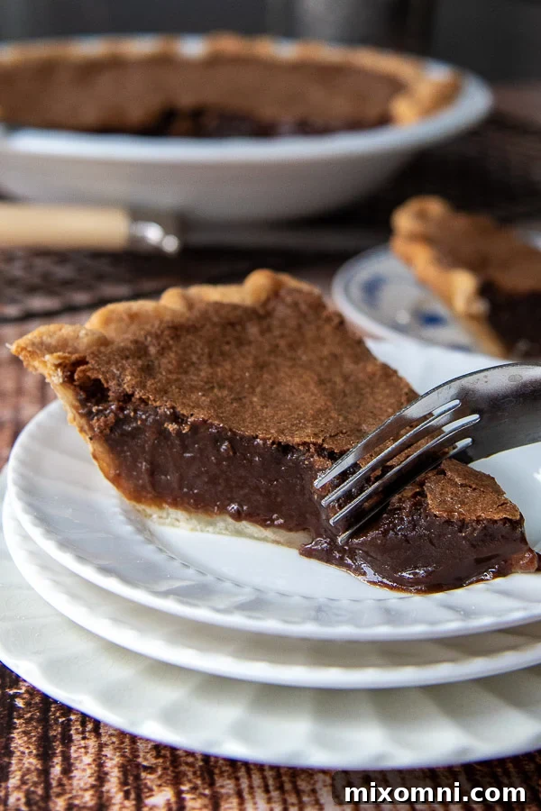 A fork cutting into a piece of chocolate chess pie, showcasing its rich, fudgy interior and flaky crust.