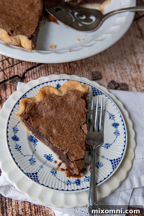 An overhead shot of a luscious slice of chocolate chess pie, resting on a charming blue and white plate, with a fork poised nearby.