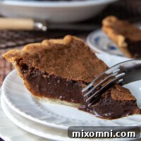 A fork cutting into a piece of chocolate chess pie, revealing its rich, fudgy interior.