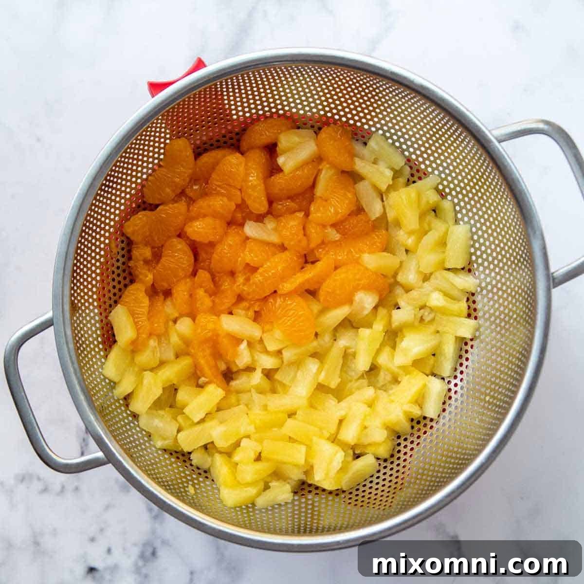 Pineapple tidbits and mandarin oranges draining in a colander to remove excess liquid.