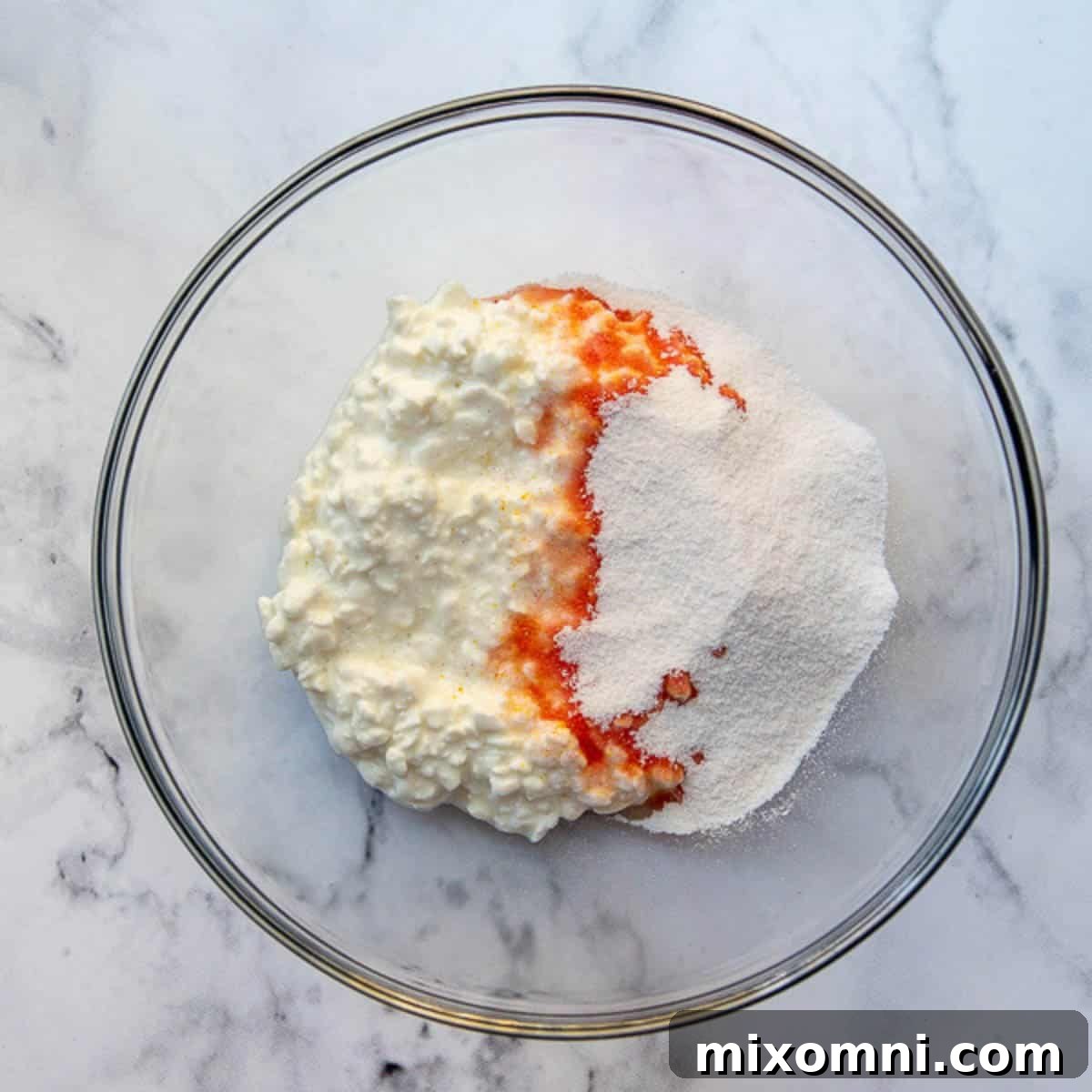 Orange jello powder being dissolved into cottage cheese in a mixing bowl.