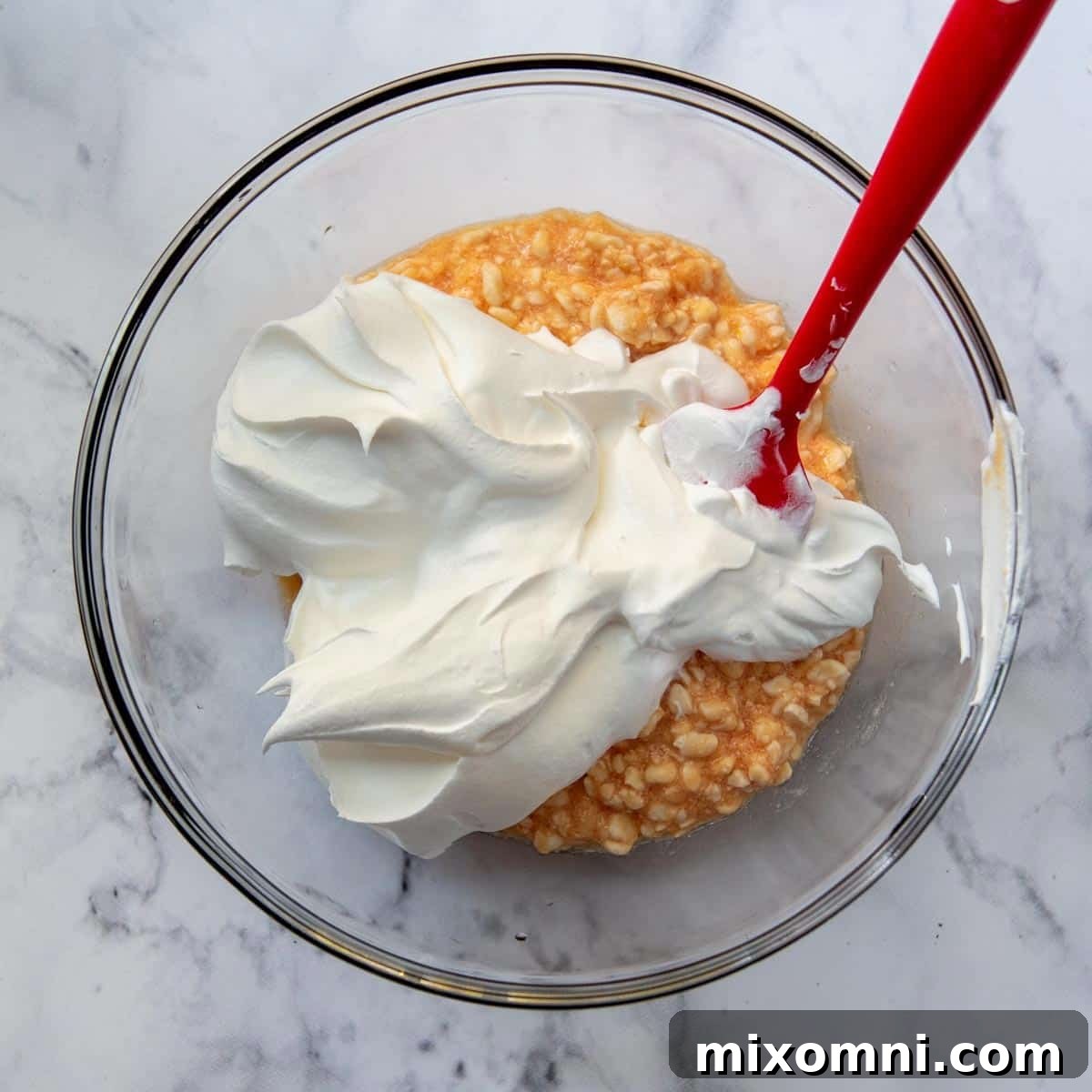 Cool Whip whipped topping being gently folded into the orange jello and cottage cheese mixture.