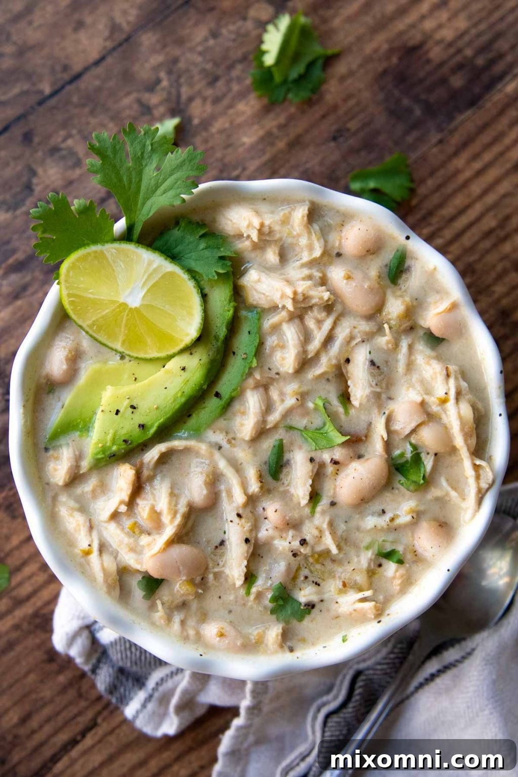 Overhead shot of Instant Pot white chicken chili with sliced avocados, cilantro, and lime wedge on top