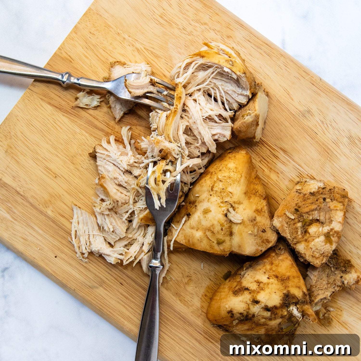 Chicken being shredded on a cutting board.