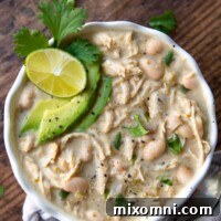 overhead shot of instant pot white chicken chili with sliced avocados, cilantro, and lime wedge on top