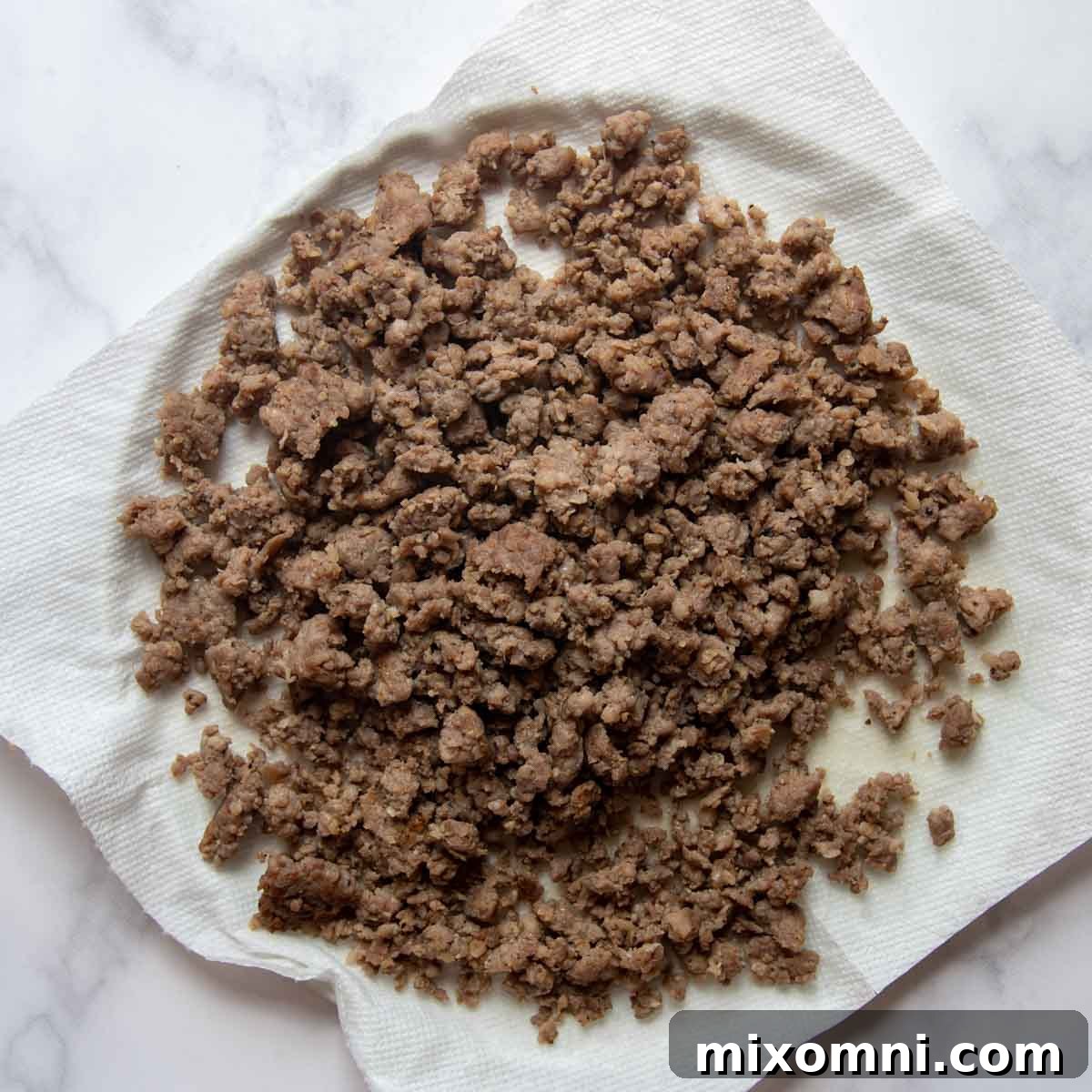 Crumbled, browned breakfast sausage resting on a paper towel-lined plate, ready to be added to the muffin batter.