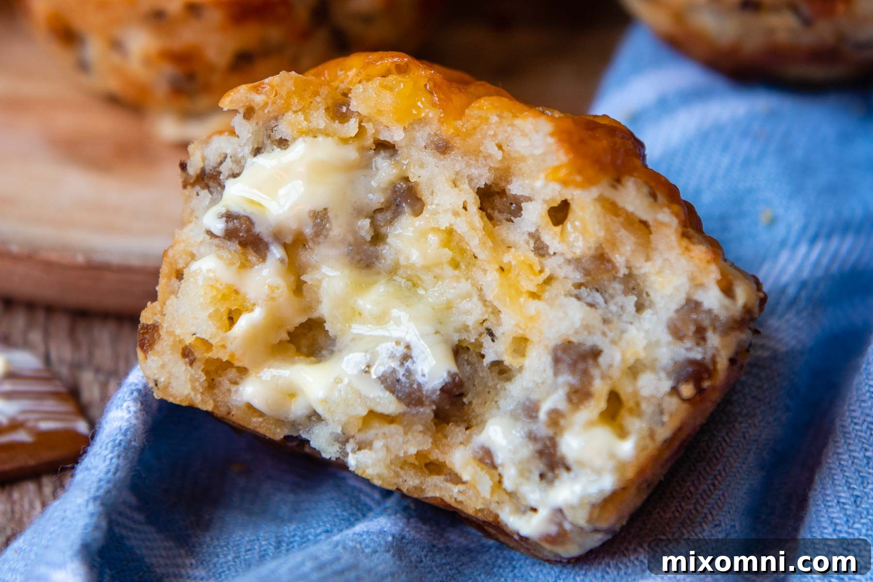 A warm sausage muffin split open, revealing melted cheddar cheese and savory sausage chunks, with a pat of butter melting on top.
