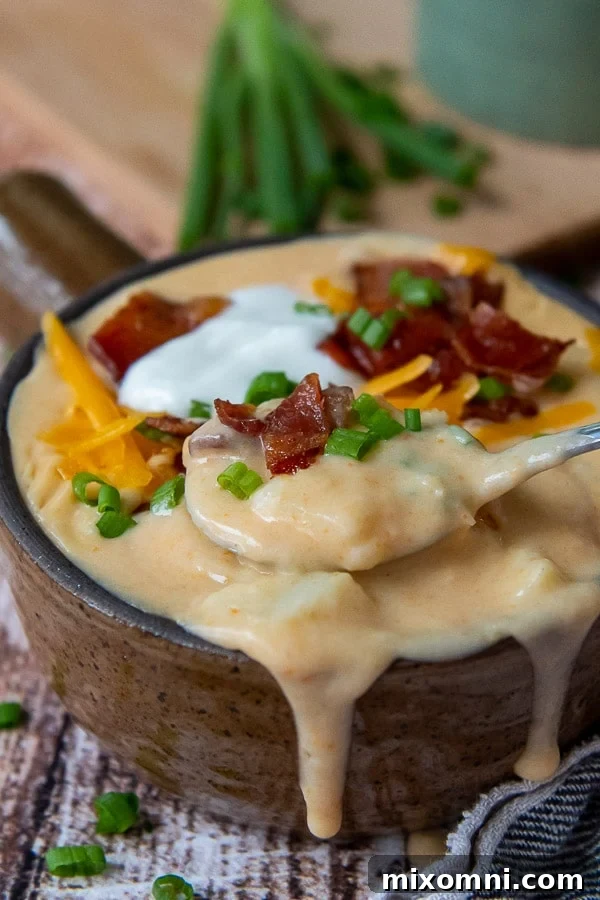 A close-up shot of a spoon lifting a spoonful of rich, creamy Instant Pot Loaded Potato Soup from a bowl, garnished with bacon and chives.
