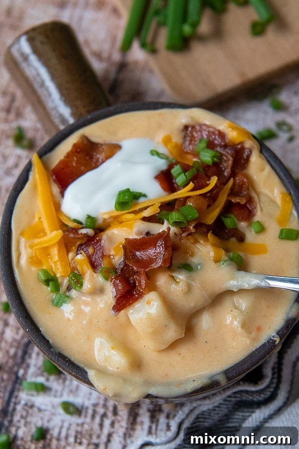 A close-up of a spoon dipping into a bowl of creamy Instant Pot Loaded Potato Soup, showing the rich texture.