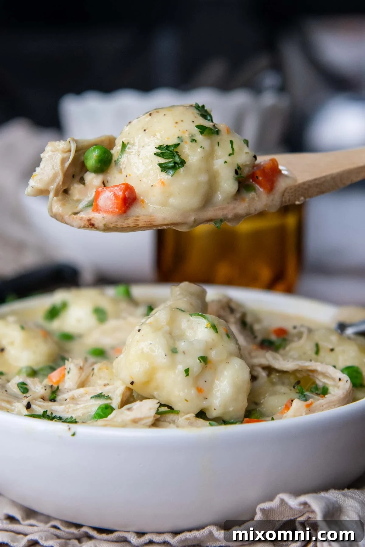 A wooden spoon holding up a scoop of thick, creamy chicken and dumplings, showcasing the tender chicken, vegetables, and fluffy gluten-free dumplings.
