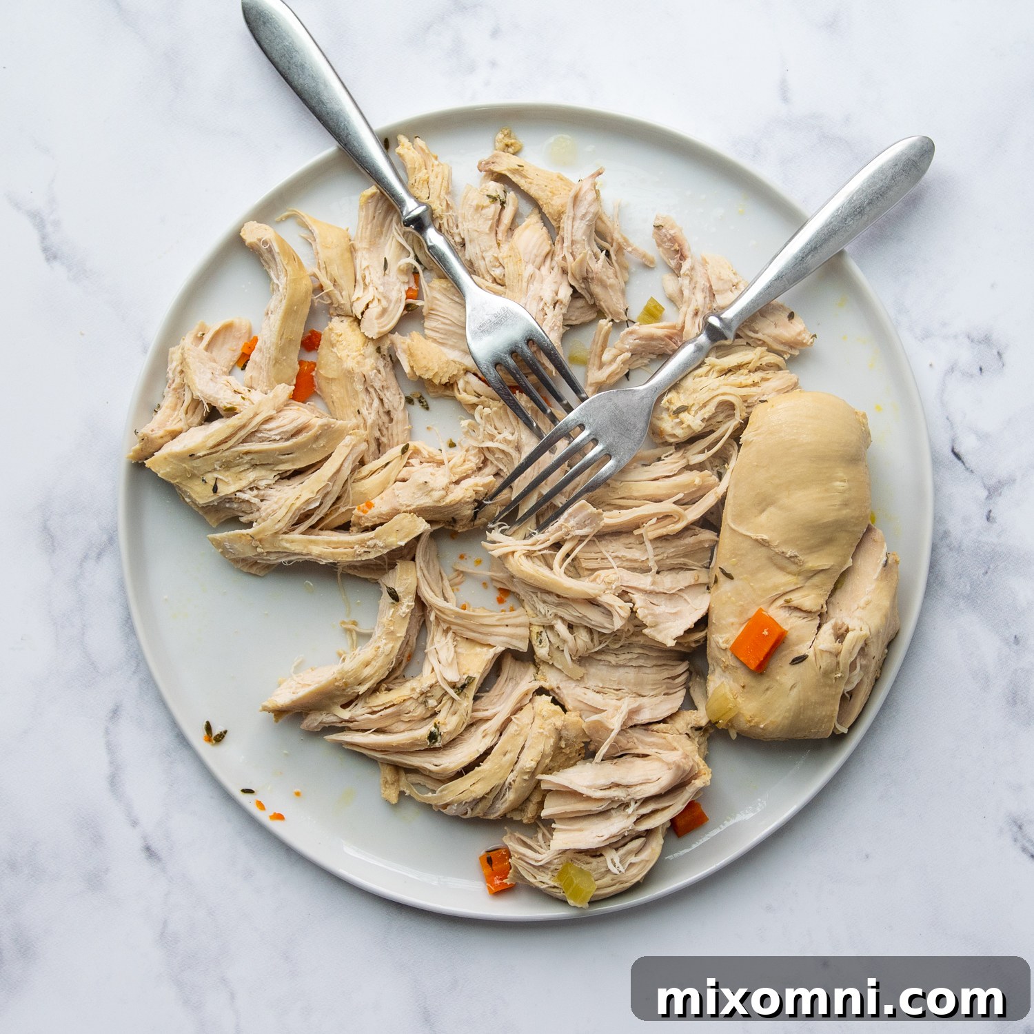 Cooked chicken breasts being shredded into bite-sized pieces on a white plate, ready to be added back to the soup.