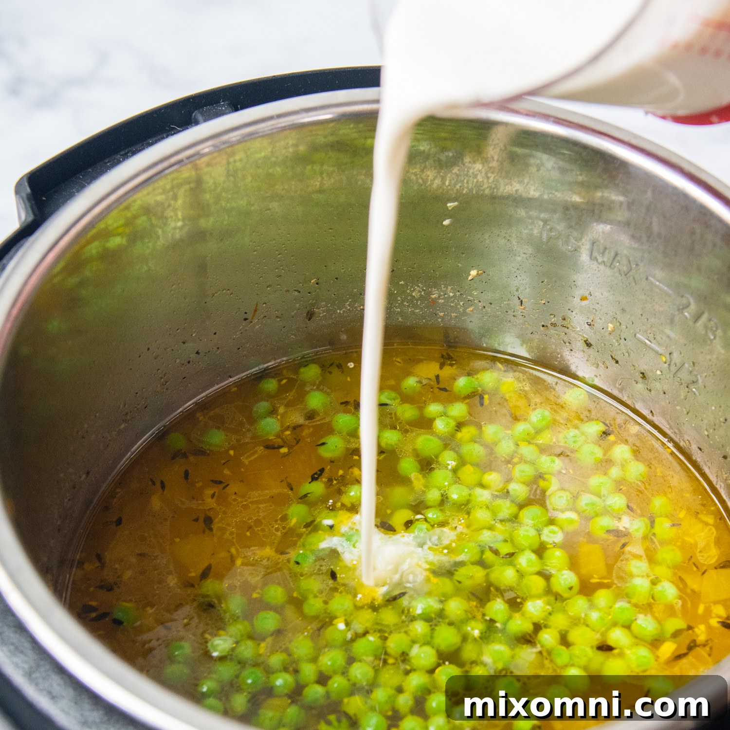 Heavy cream mixed with cornstarch being poured into the simmering chicken soup, ready to be stirred for thickening.