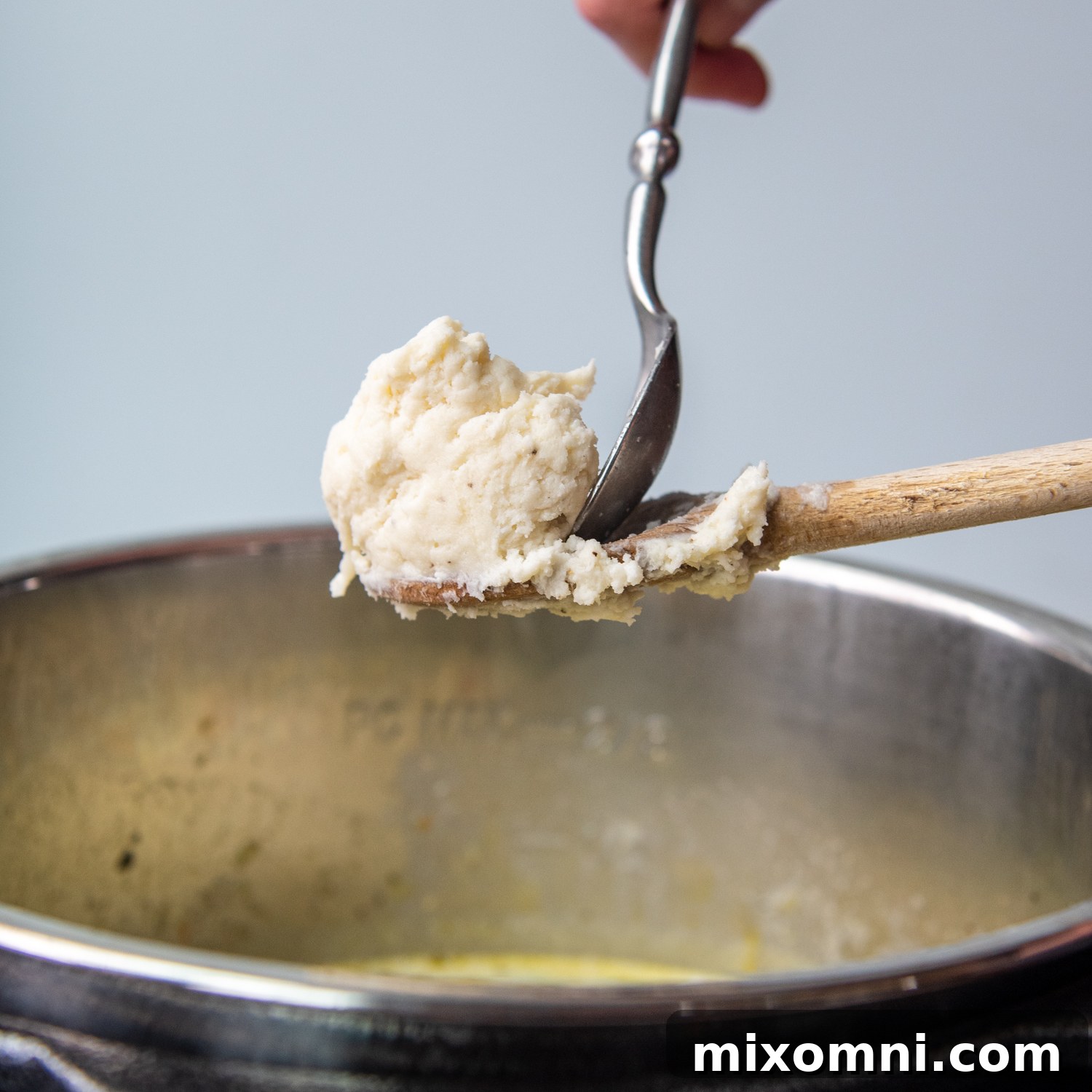 A small cookie scoop or spoon scraping gluten-free dumpling dough into the simmering Instant Pot chicken soup.