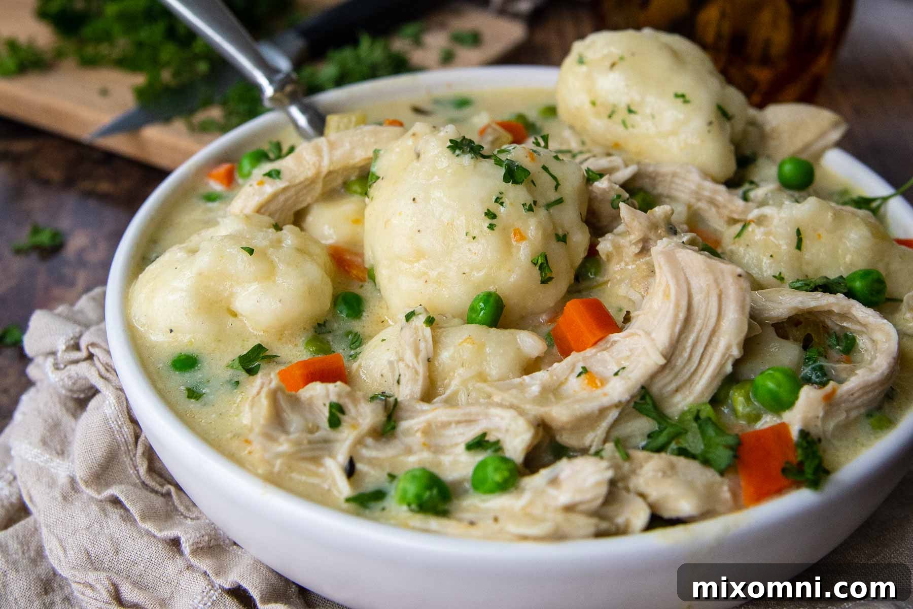 Close-up side angle shot of a deep white bowl filled with creamy Instant Pot gluten-free chicken and dumplings, highlighting the texture and richness.