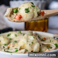 A wooden spoon holding up a scoop of creamy chicken and dumplings with tender gluten-free dumplings, ready to be served.