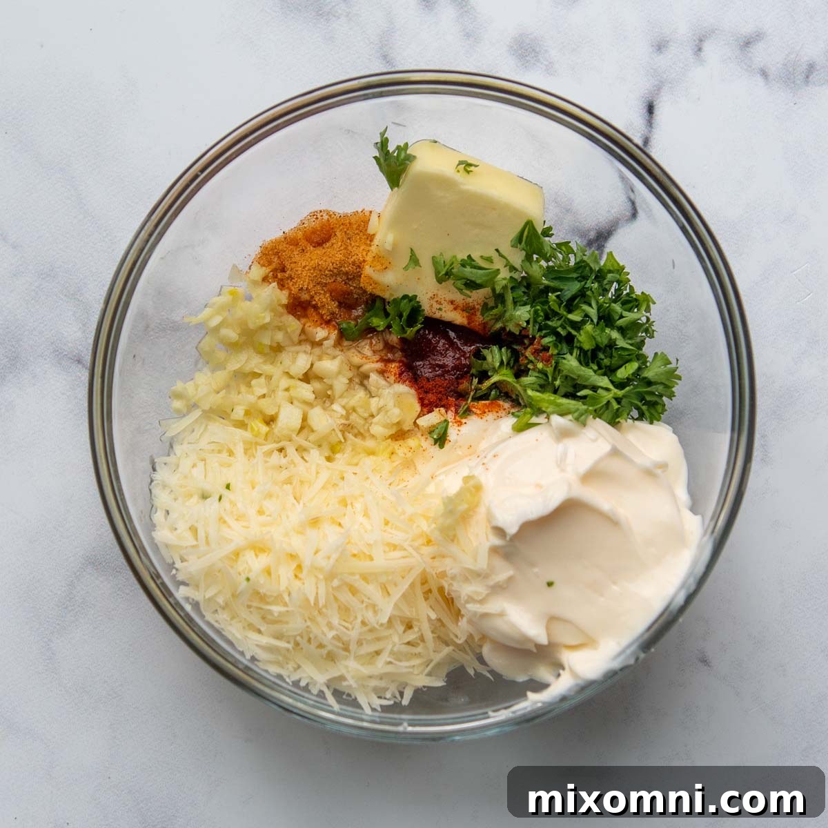 All ingredients for the creamy parmesan topping mixed together in a clear glass bowl