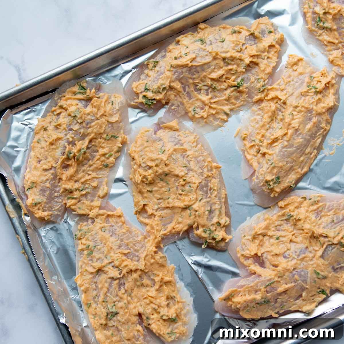 The creamy lemon garlic mayo and parmesan topping being evenly spread over the tilapia fillets