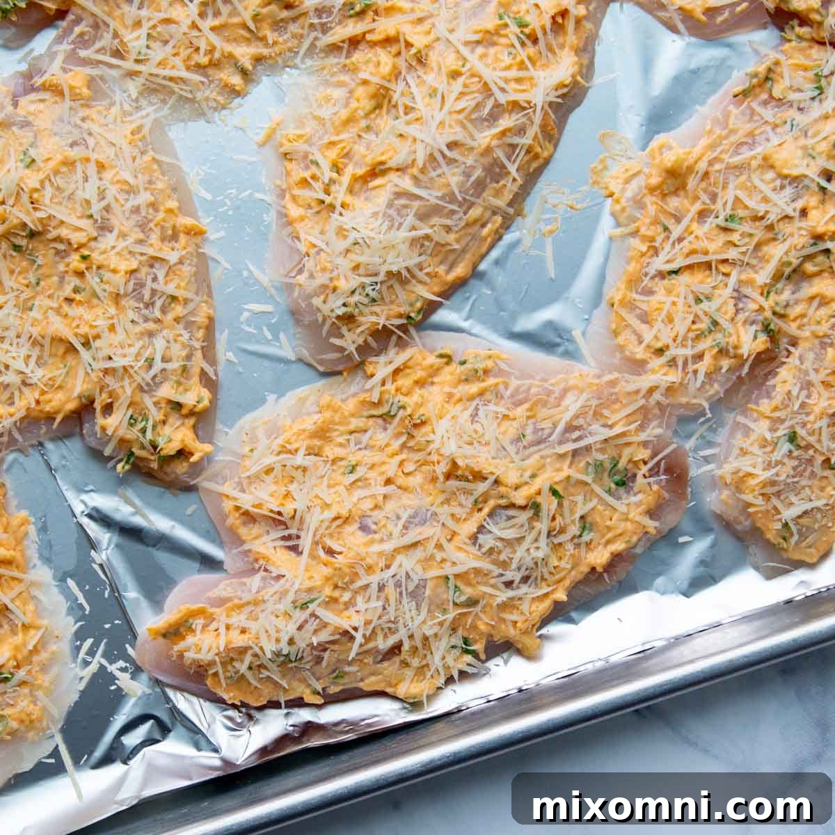 Extra grated parmesan cheese being sprinkled generously over the topping on the tilapia fillets before baking