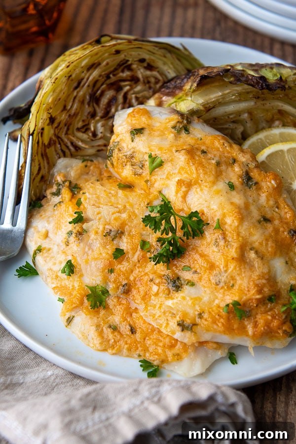 A perfectly cooked piece of Parmesan Crusted Tilapia on a white plate with a fork nearby, showing the golden-brown crust