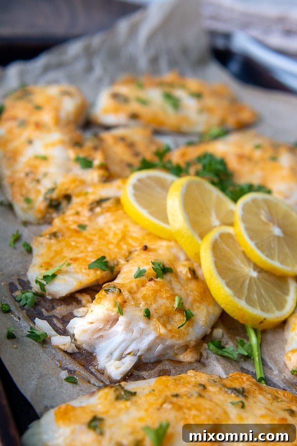 Close-up of a broken piece of Parmesan Crusted Tilapia on a baking sheet, revealing the flaky white fish and crispy crust