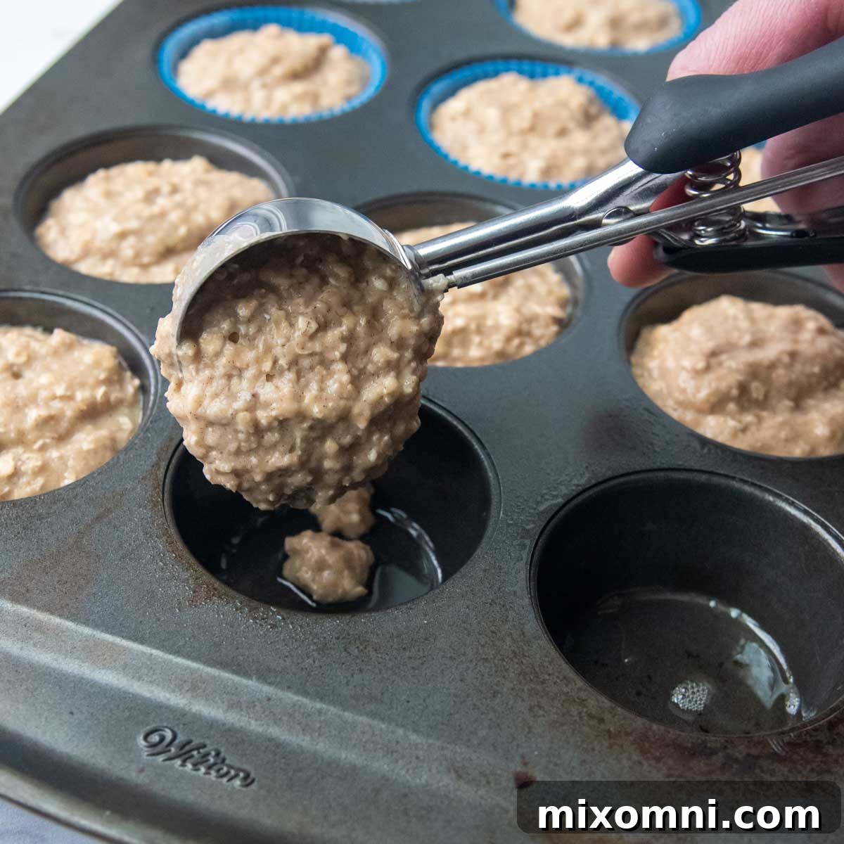 Muffin batter being scooped into muffin tins using a trigger scoop for even portions.