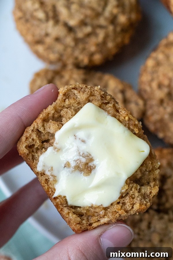 A half-eaten applesauce oatmeal muffin with a dollop of melted butter on top, showcasing its soft interior and inviting warmth.