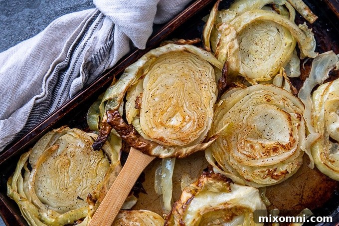 a wooden spatula holding up a roasted cabbage slice from a sheet pan, showcasing its golden brown and crispy texture