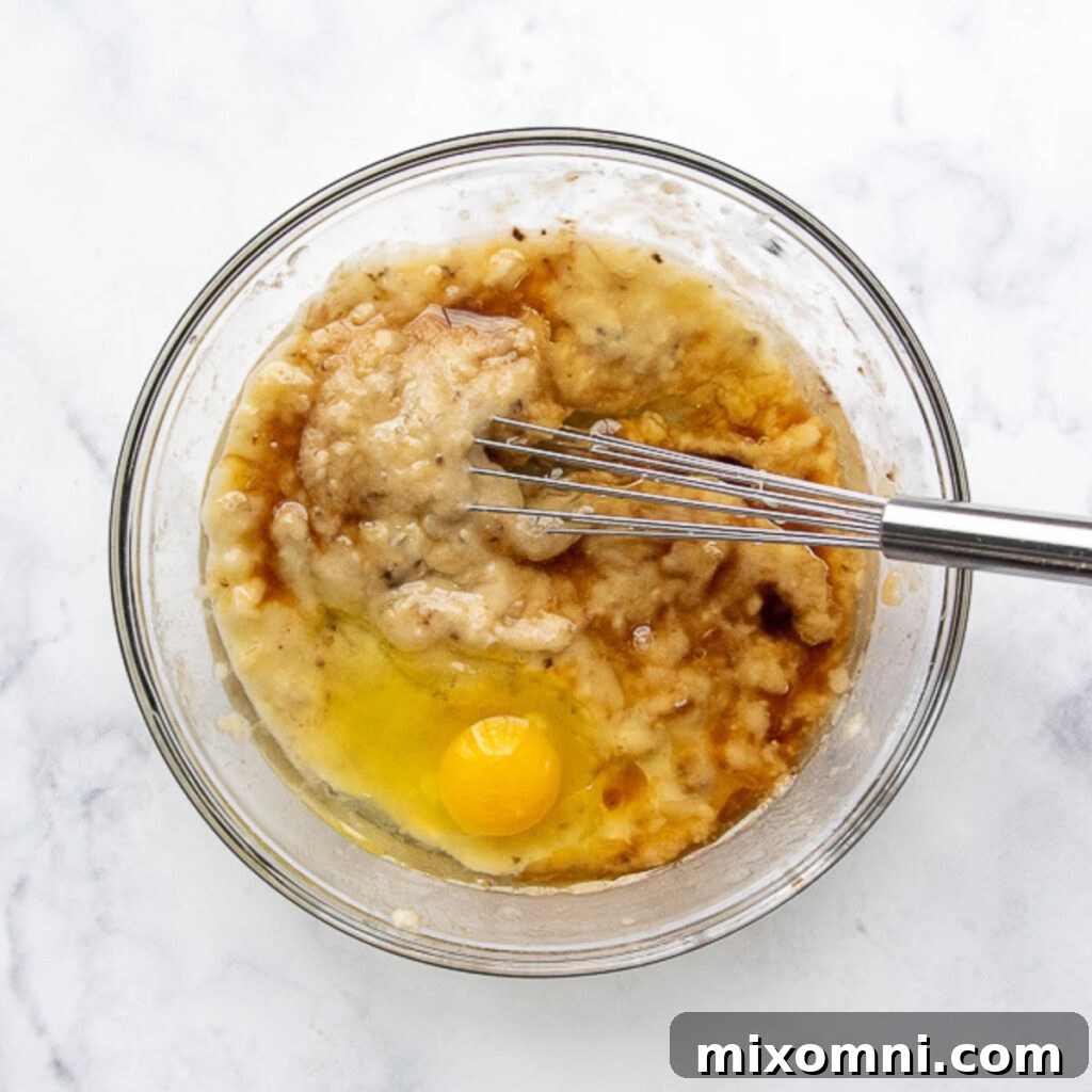 Mashed bananas being whisked with other wet ingredients in a bowl.