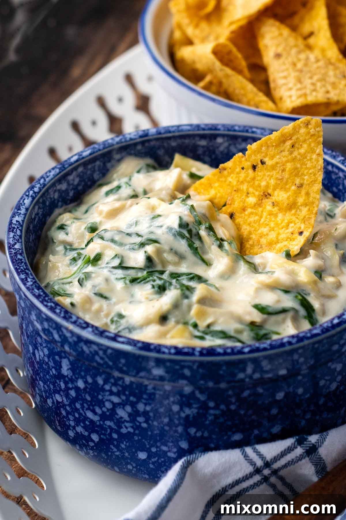 A crisp tortilla chip rests invitingly in a bowl of hot, creamy spinach artichoke dip, ready to be enjoyed.