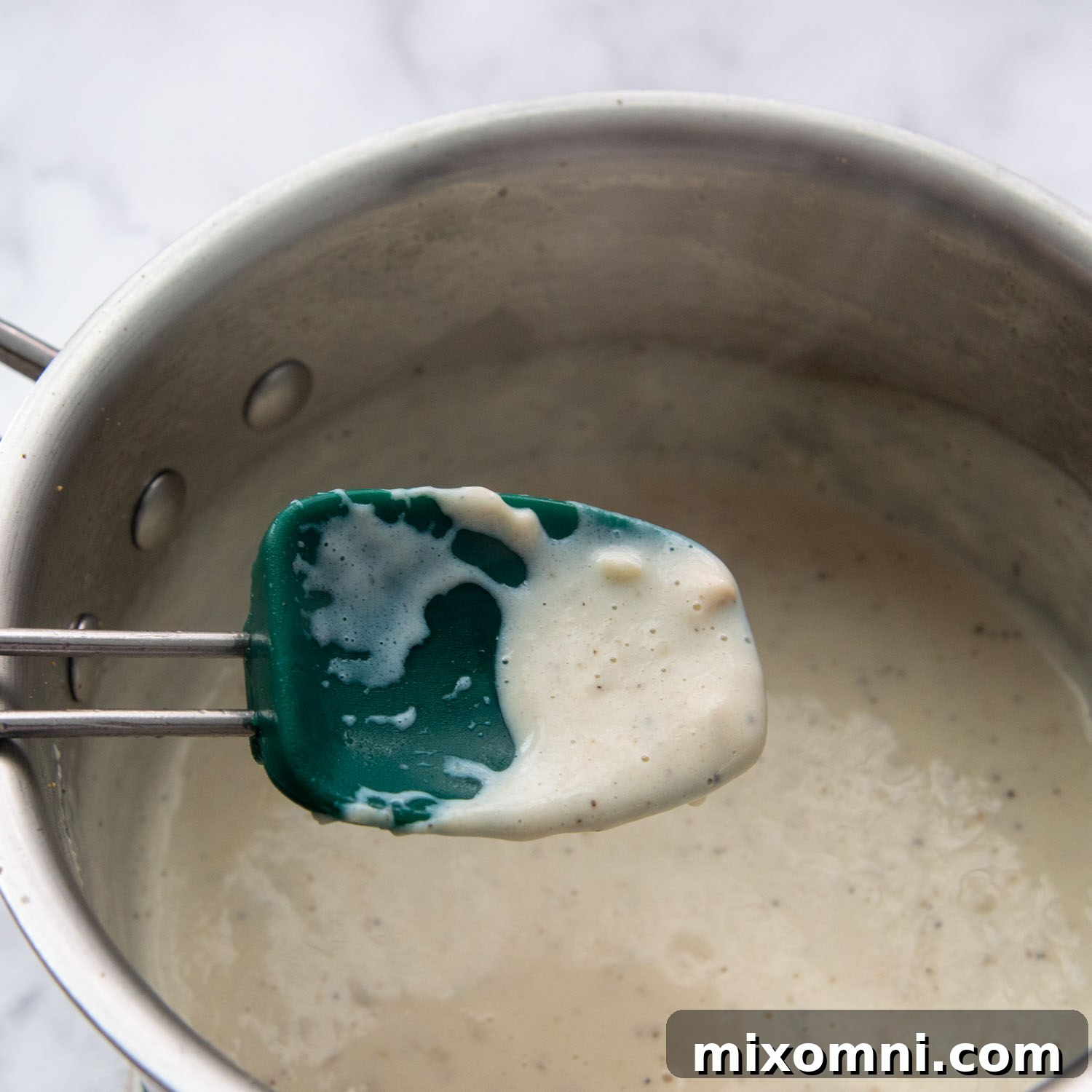 A spoon lifts a portion of the thickened cream sauce, demonstrating its rich consistency.