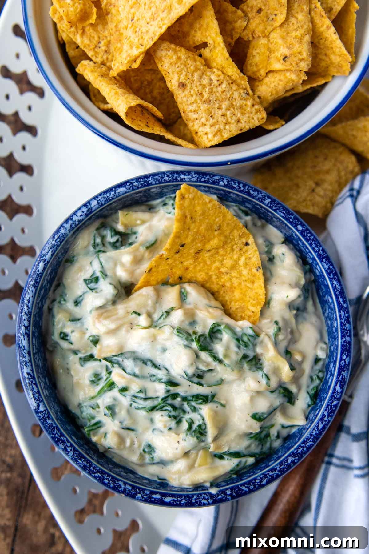 An overhead shot showcasing a vibrant blue bowl filled with a generous serving of creamy spinach artichoke dip, garnished and ready to be devoured.