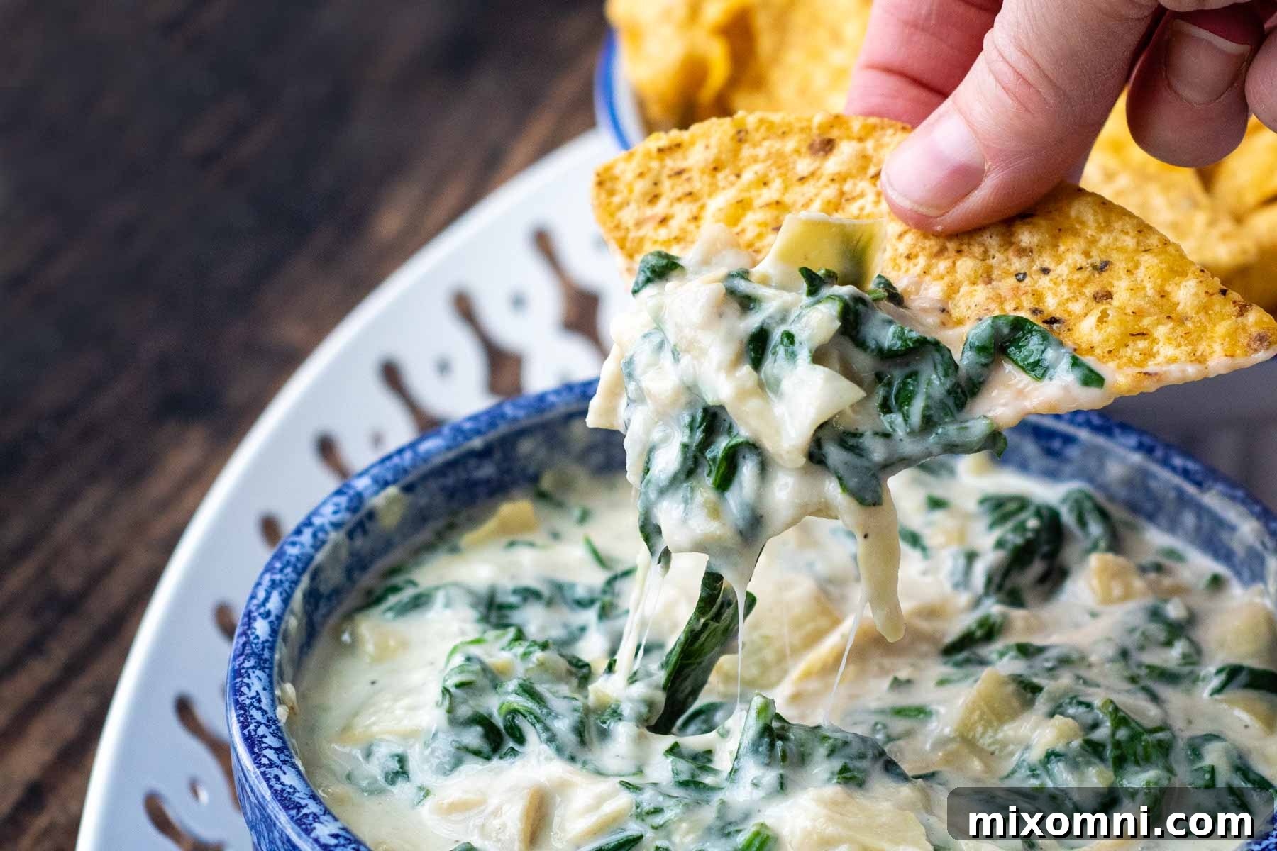 A hand dipping a crispy tortilla chip into the luscious, hot spinach artichoke dip, highlighting its perfect dipping consistency.