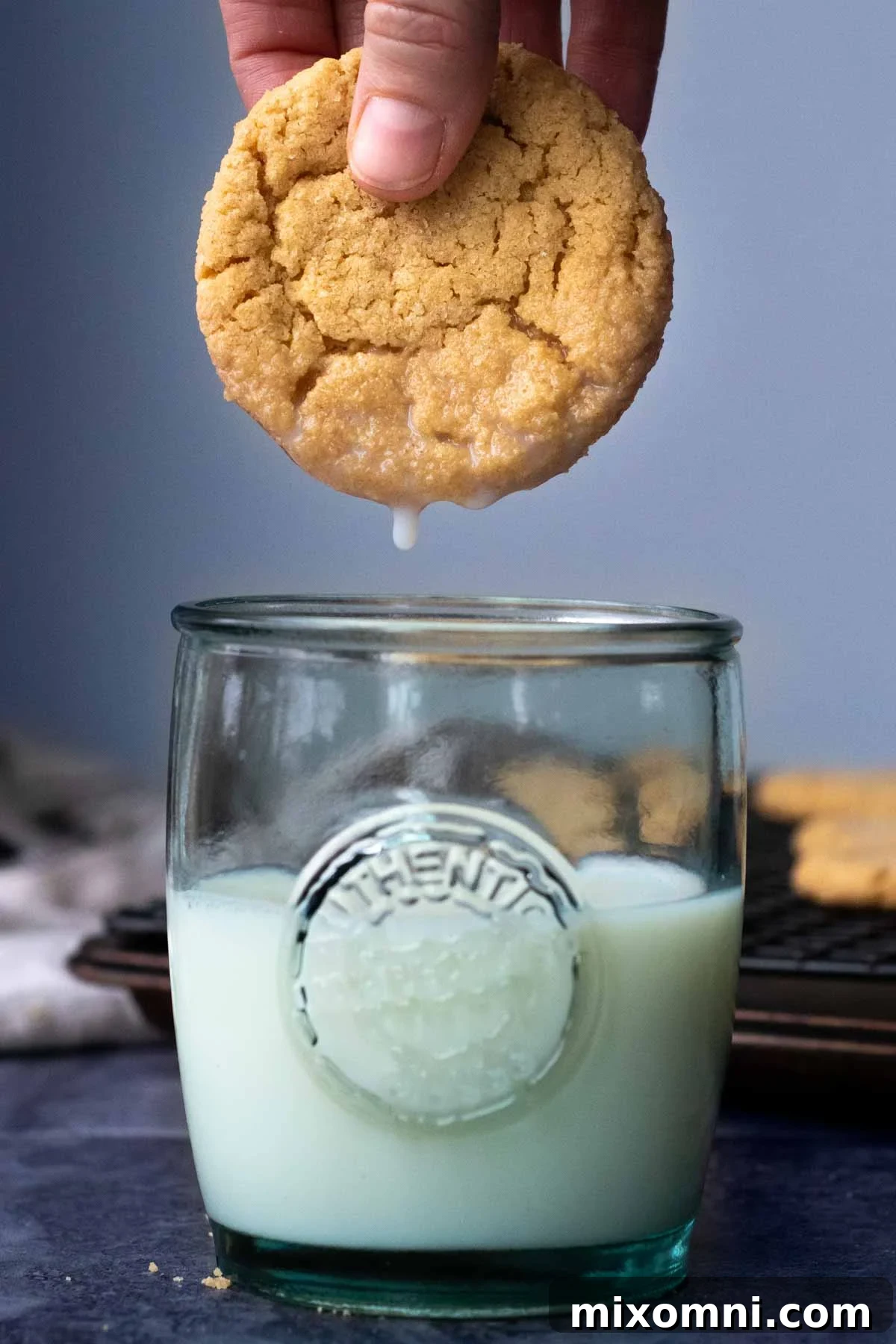 A perfectly baked almond flour peanut butter cookie being dipped into a refreshing glass of milk, highlighting its soft texture.