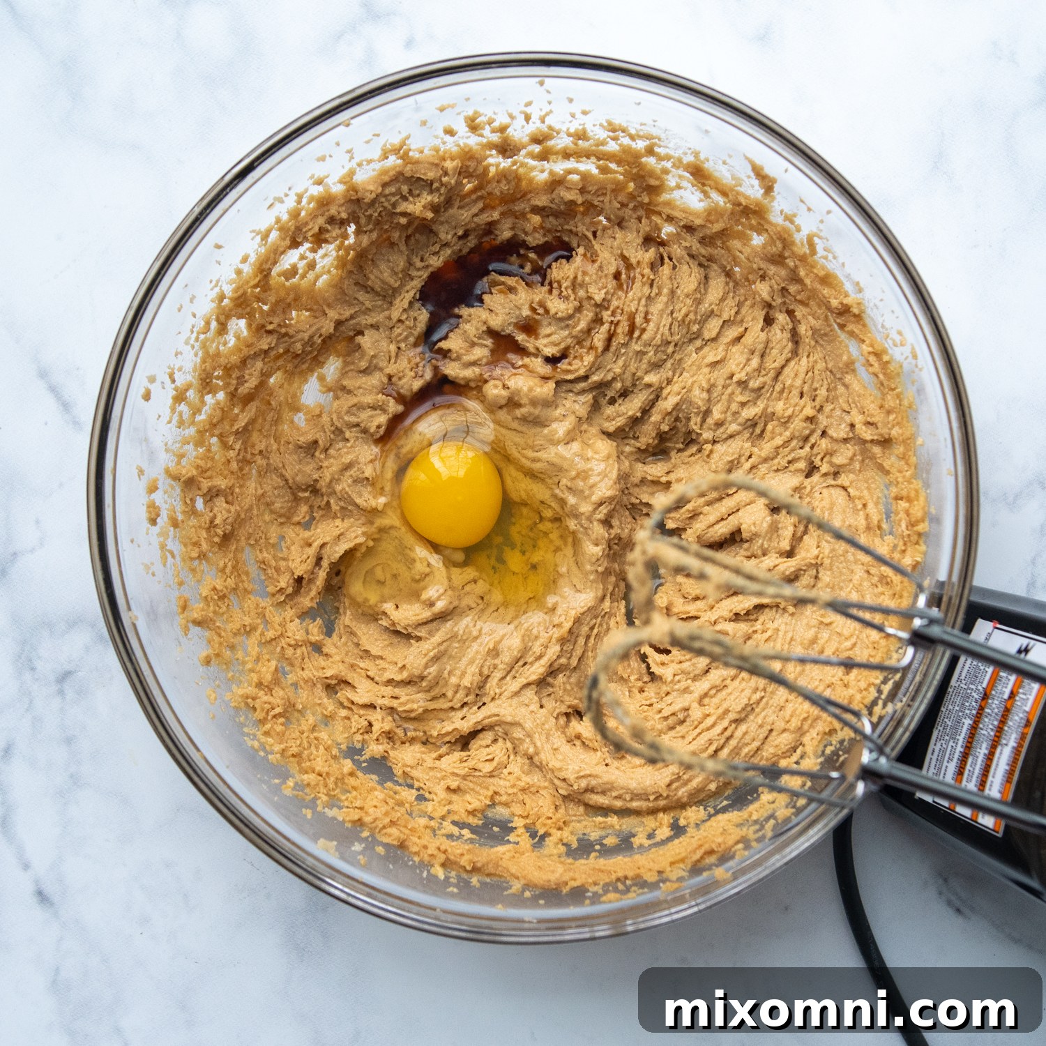 The smooth, creamy peanut butter cookie dough in a mixing bowl, with a single egg just added, ready to be incorporated.