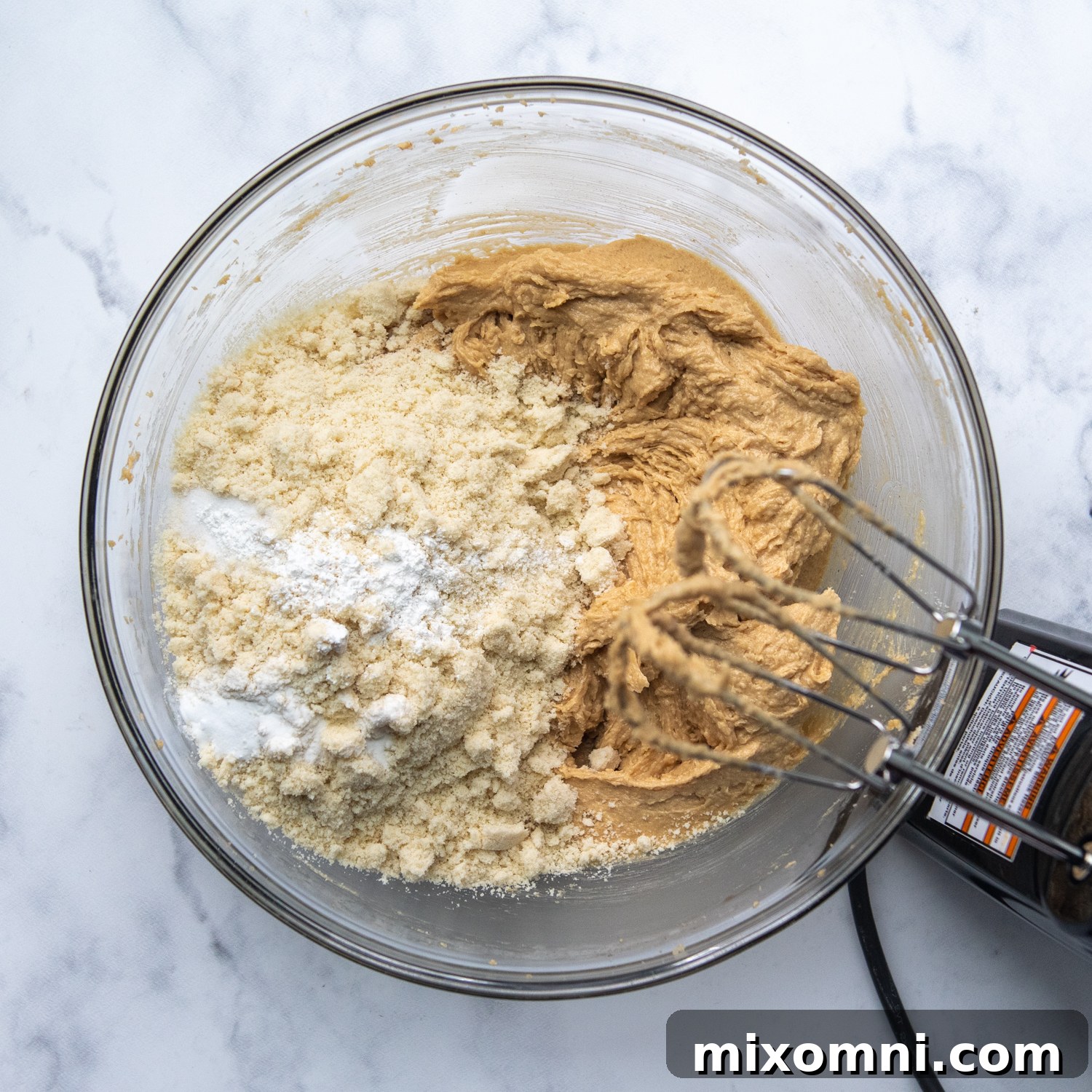 Finely blanched almond flour being gently mixed into the creamy peanut butter and sugar mixture, forming the cookie dough.
