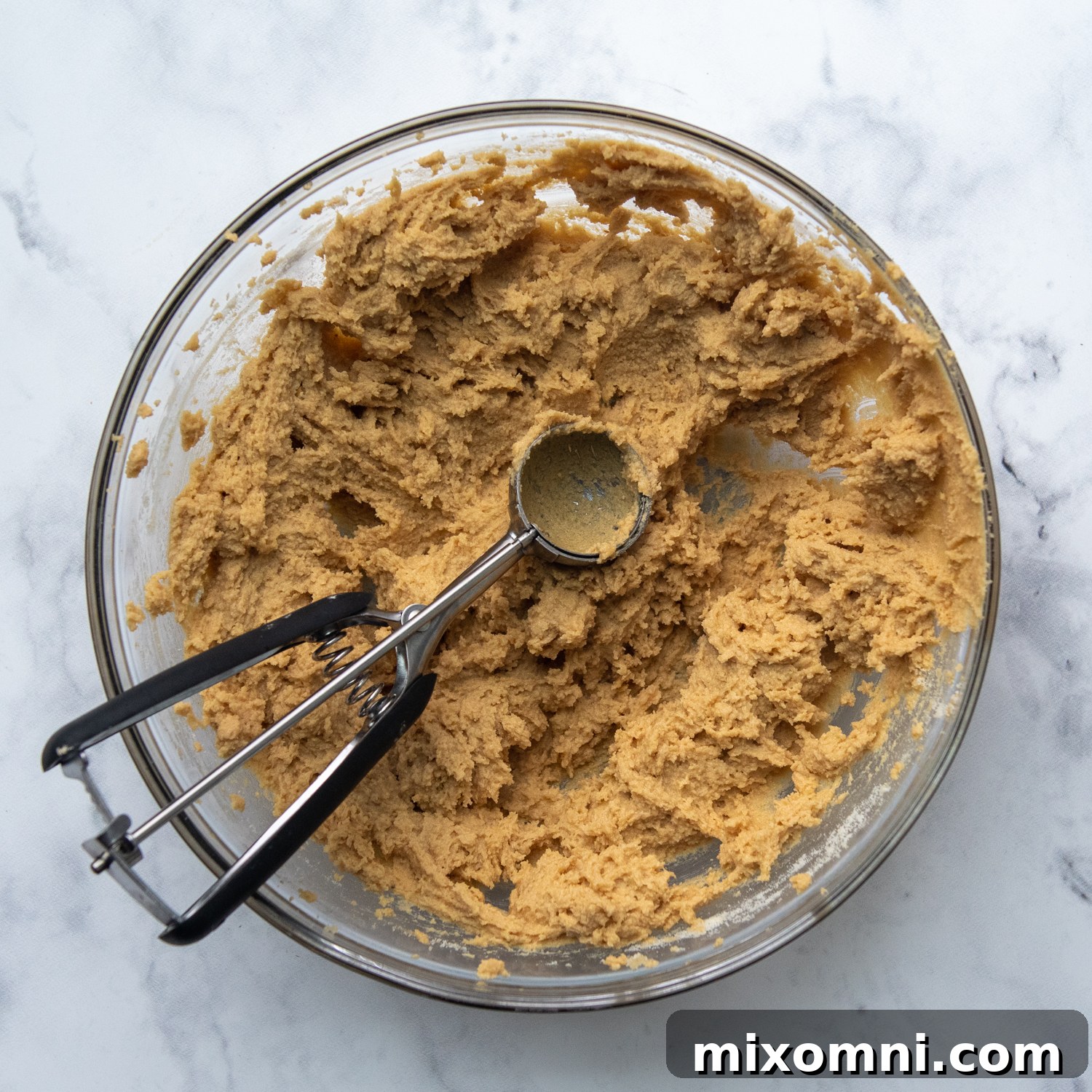 A small cookie scoop perfectly portioning out the rich peanut butter cookie dough directly from the mixing bowl, ready for baking.